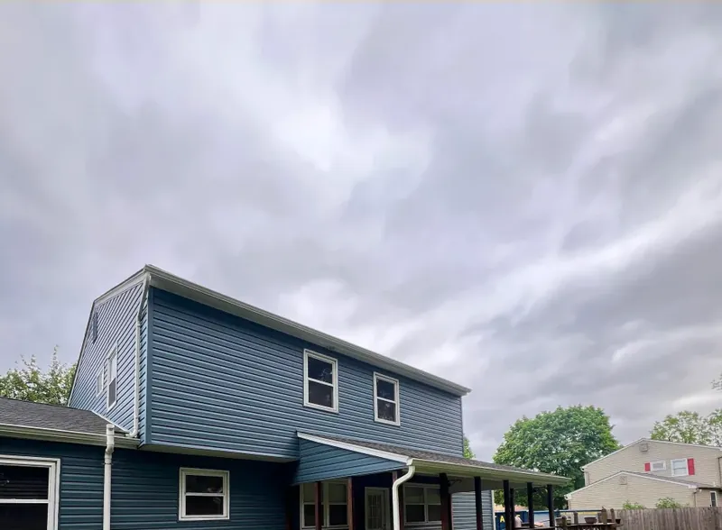 Two-story home clad in dark blue vinyl siding with white trim and a new gutter line, under a grey sky.