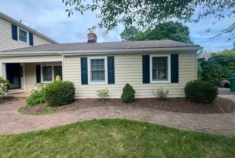 Single-story home finished in cream vinyl siding with dark blue shutters and a brick walkway.